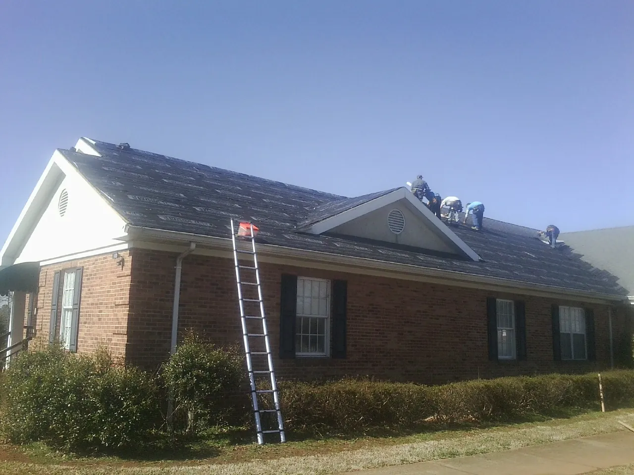 Crew tearing shingles off a brick ranch roof with a ladder set — Emergency Roof Repair work by our crew in Lutts