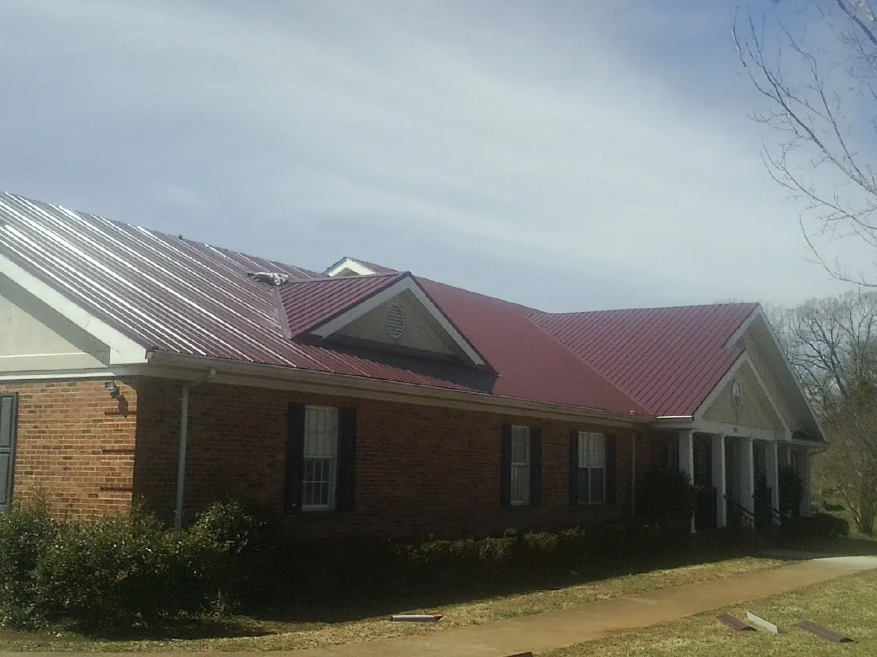 Red metal roof with gabled entries on a long brick building, from a Hail Damage Roof Repair job in Lutts