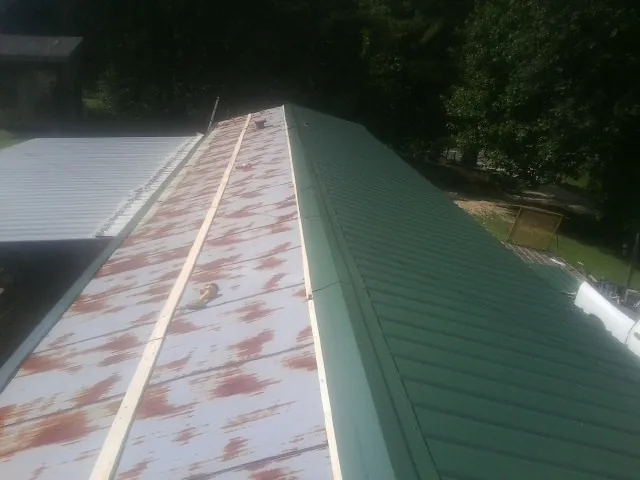 Old rusted panels beside newly installed green metal roofing — Wind Damage Roof Repair by Roofing Brothers in Lutts