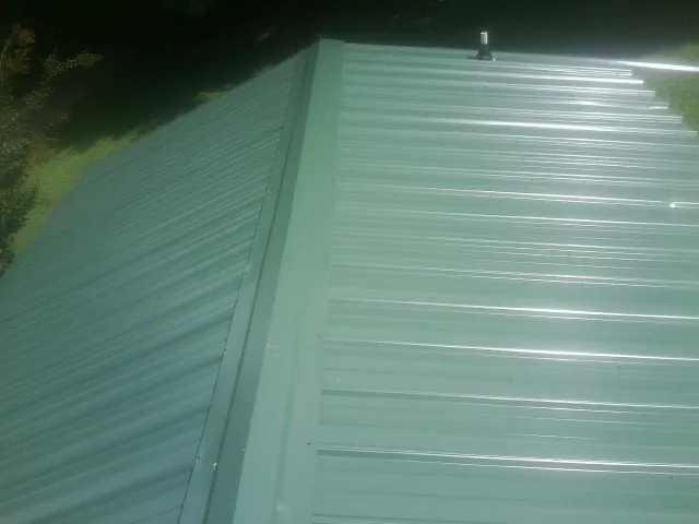New green metal panels meeting at the ridge of a roof — Flat Roof Repair work by our crew in Lutts