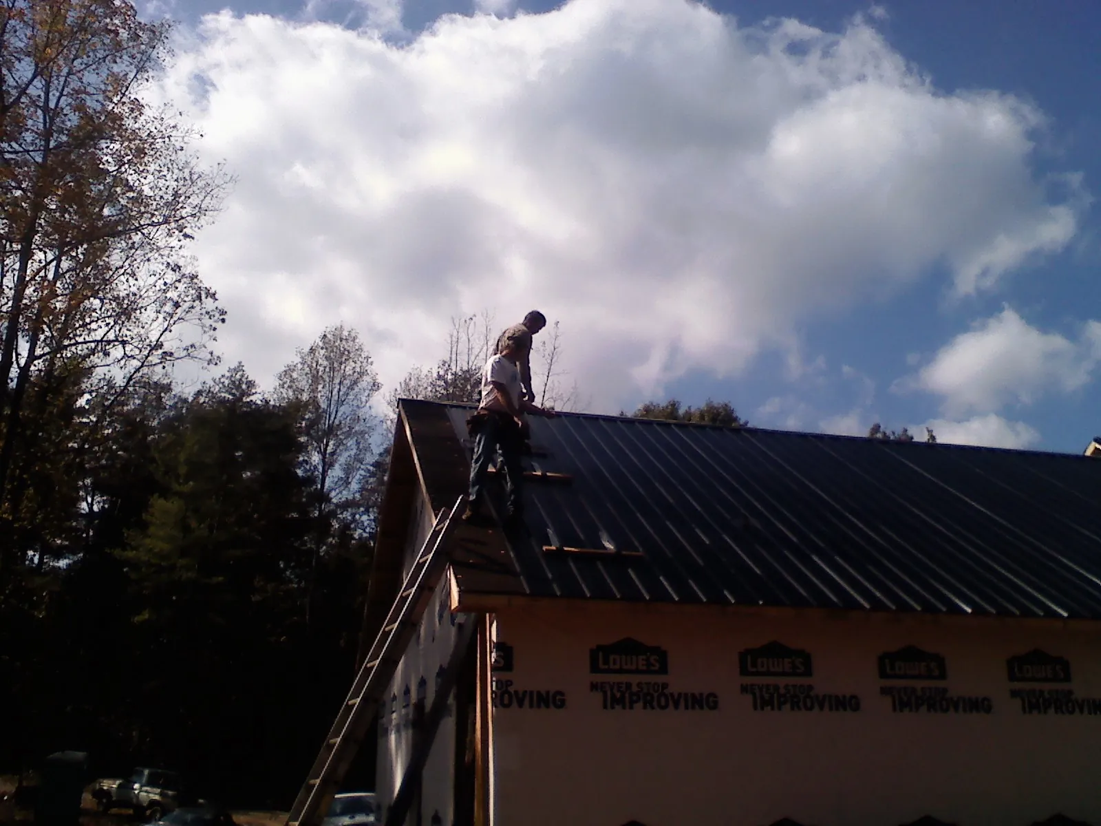 Roofer fastening dark metal panels high against a cloudy sky, from a Roof Inspection job in Lutts