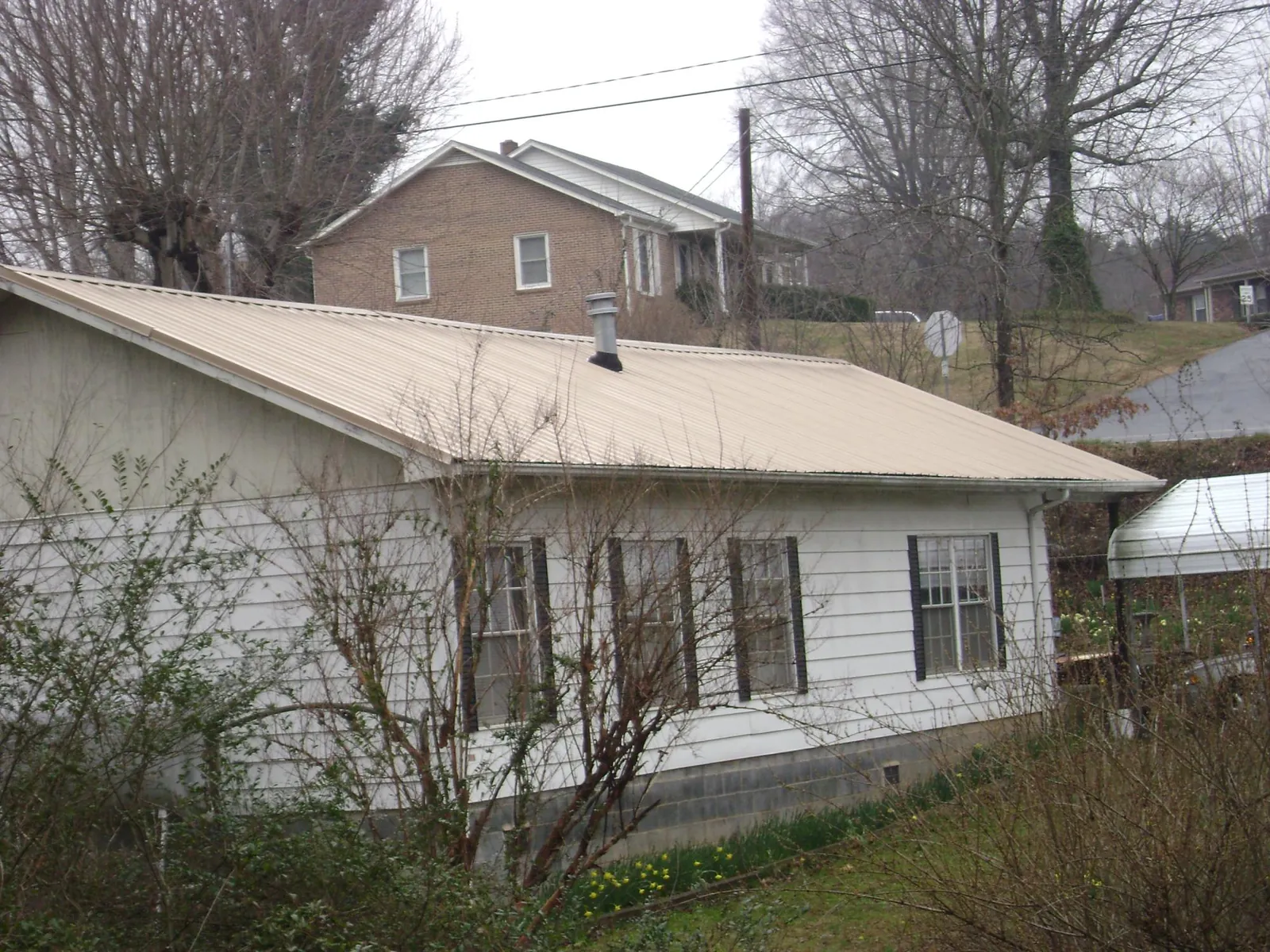Tan metal roof on a white sided house set into a hillside — Commercial Roofing by Roofing Brothers in Lutts
